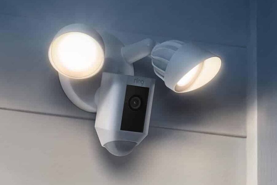 A Ring security camera with two bright floodlights is mounted on an exterior wall, illuminating the area.
