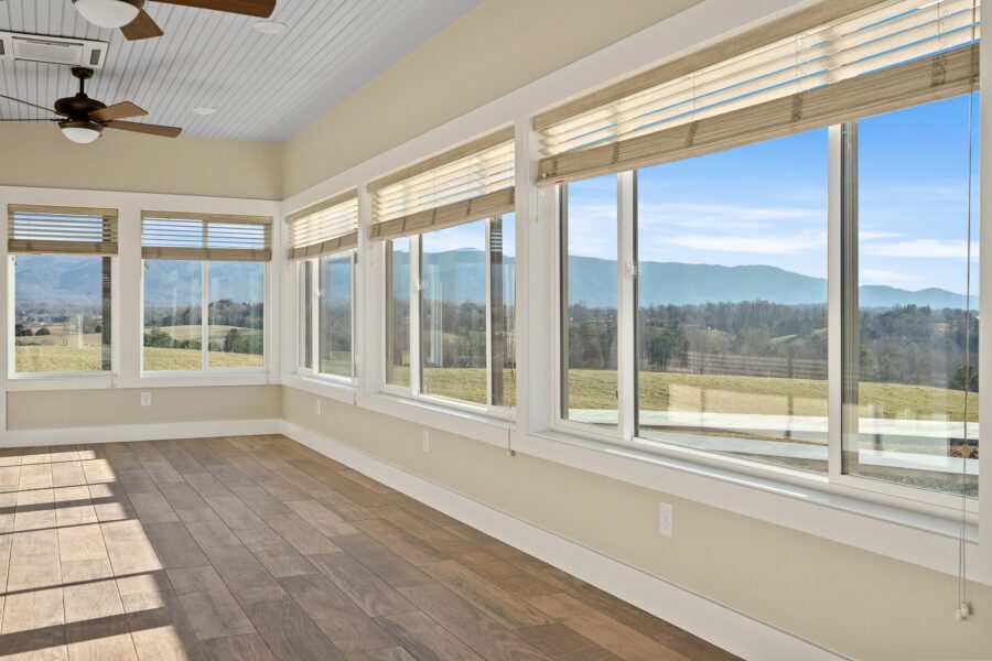 Bright sunroom with large windows, wood floors, and ceiling fans, offering a scenic view of rolling hills and blue mountains under a clear sky.